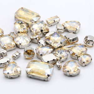 Puede incluir: Una variedad de piedras de cristal transparentes y ámbar con engastes plateados. Las piedras de cristal son de diferentes formas, incluyendo redonda, cuadrada, ovalada y de corazón.