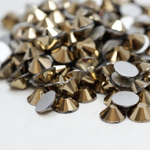 May include: A pile of gold-colored rhinestones, some with silver backs, scattered on a white surface.