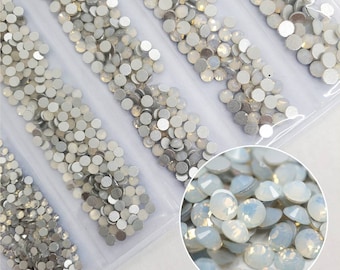 May include: A close-up of a package of iridescent white round rhinestones. The rhinestones are arranged in rows on a white background.