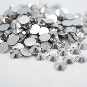 May include: A pile of silver-coloured rhinestones, some with a flat back and some with a faceted design.