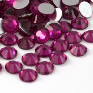 May include: A close-up of a pile of small, round, magenta-colored rhinestones.