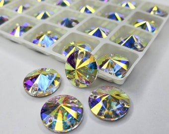 May include: A collection of iridescent, round rhinestones with a flat back and two holes for sewing. The rhinestones are displayed in a white plastic tray with individual compartments, and some are scattered outside the tray.