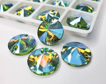 May include: A collection of round, green iridescent rhinestones with a pointed center. The rhinestones are arranged on a white surface.