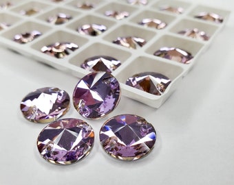 May include: Oval-shaped, faceted, light purple rhinestones. Some rhinestones are loose, while others are in a white plastic organizer with multiple compartments. The rhinestones have a shiny, reflective surface.