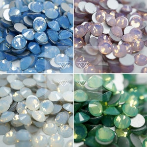 Puede incluir: Cuatro secciones de piedras preciosas iridiscentes y facetadas en tonos azul claro, rosa pálido, blanco y verde. Cada gema tiene un reverso plano plateado. Las gemas están dispersas, creando un efecto texturizado y brillante. Ideal para la fabricación de joyas y manualidades.