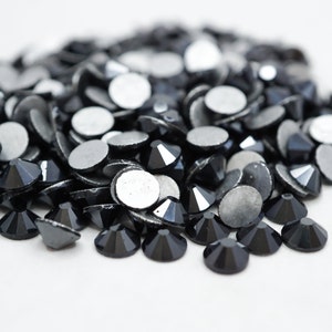 Puede incluir: Un montón de pedrería negra con respaldos plateados. La pedrería está esparcida sobre una superficie blanca.