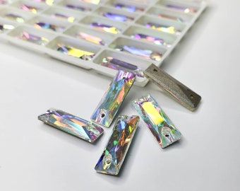 May include: Assortment of iridescent rectangular rhinestones with a hole in the center. The rhinestones are scattered on a white surface.