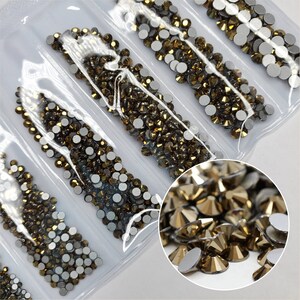 Puede incluir: Primer plano de un paquete de piedras de cristal de color dorado. Las piedras de cristal están dispuestas en filas y están empaquetadas en plástico transparente. Las piedras de cristal son pequeñas y tienen una parte posterior plana.