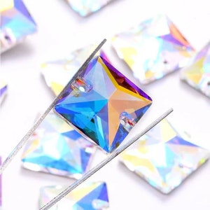 May include: Assortment of iridescent square-shaped rhinestones with two holes in each. The rhinestones have a rainbow effect with shades of blue, purple, and yellow.