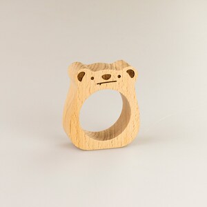 May include: A wooden napkin ring shaped like a bear with a simple face carved into it.