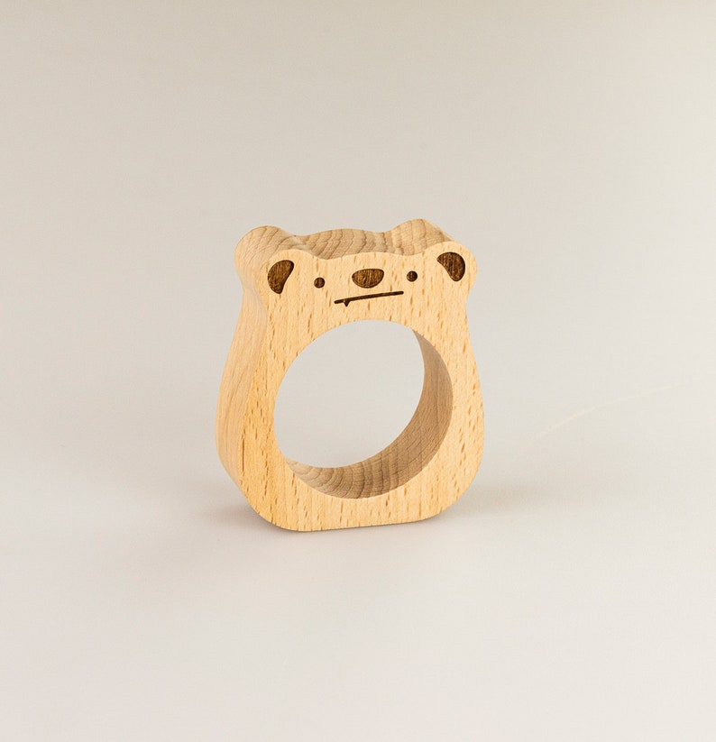 May include: A wooden napkin ring shaped like a bear with a simple face carved into it.