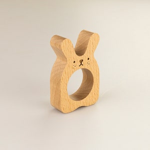 May include: Wooden bunny napkin ring with a carved face and a hole in the center for holding napkins.