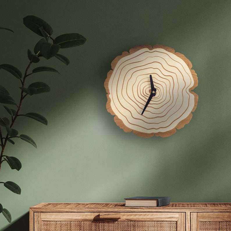Pu&ograve; includere: Un orologio in legno con un quadrante bianco e lancette nere. L'orologio ha la forma di un anello di albero e ha una finitura in legno naturale.