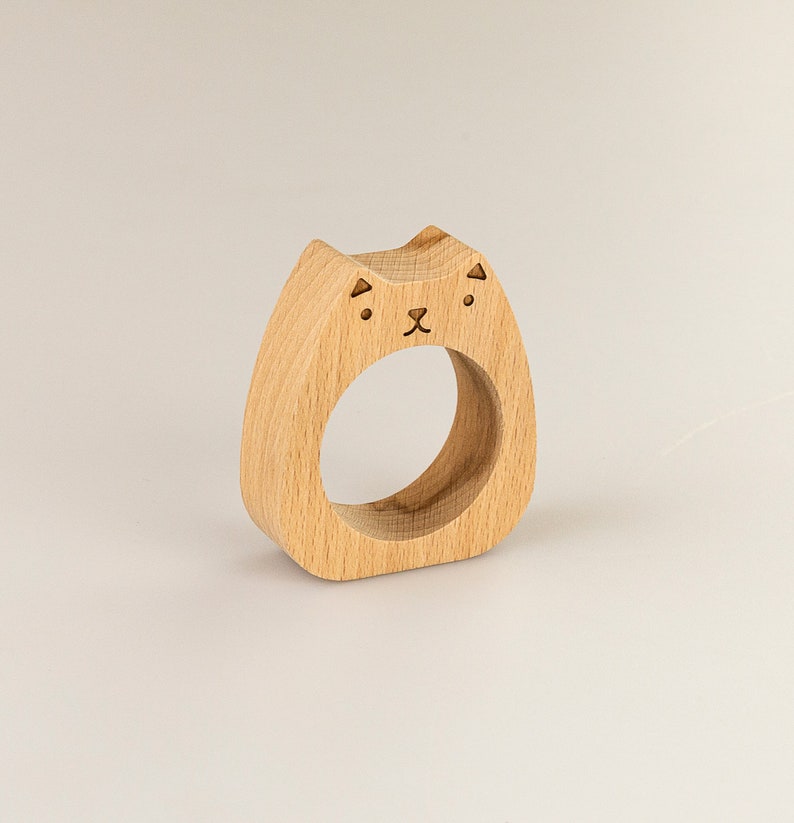 May include: Wooden napkin ring shaped like a cat with a simple face design.