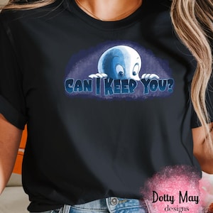 May include: A black short-sleeve t-shirt featuring a graphic of a white ghost peering over the text "CAN I KEEP YOU?" in blue letters. The design is set against a dark blue background. A pink watercolor-style logo reads "Dotty May designs".