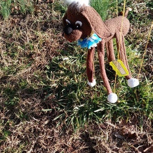May include: A brown puppet dog with white fur on its head and white feet. The puppet is hanging from strings and has a blue and white collar.