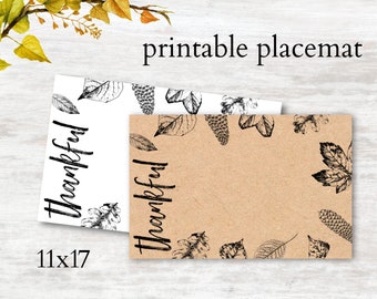May include: Printable placemat with a brown kraft paper background and black leaf designs. The text "Thankful" is written in black on both the white and brown placemats. The placemats are 11x17 inches.