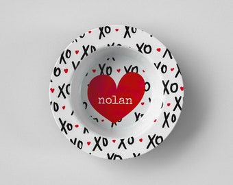 Puede incluir: Tazón de cerámica blanco con un corazón rojo y el nombre "nolan" impreso en el interior. El tazón está decorado con un patrón blanco y negro de "xo" y pequeños corazones rojos.