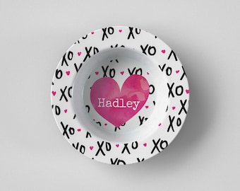 Puede incluir: Cuenco de cerámica blanco con un diseño de corazón rosa en el centro, con el nombre "Hadley". El borde del cuenco está decorado con "XO" negros y pequeños corazones rosas.
