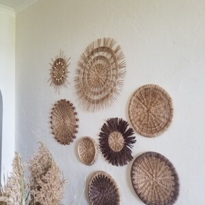May include: A wall decor set of eight woven wicker and rattan wall hangings in various shapes and sizes. The wall hangings are in shades of brown and beige and have a natural, rustic look.