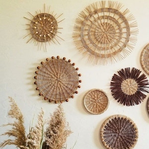 May include: A collection of six woven wall decor pieces in various shapes and sizes. The pieces are made of natural materials and have a rustic, bohemian aesthetic.