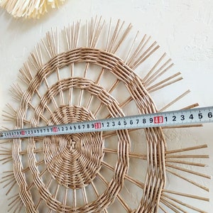 May include: A woven wall hanging with a sunburst design, measuring 40 inches in diameter. The hanging is made of natural materials and has a light brown colour.