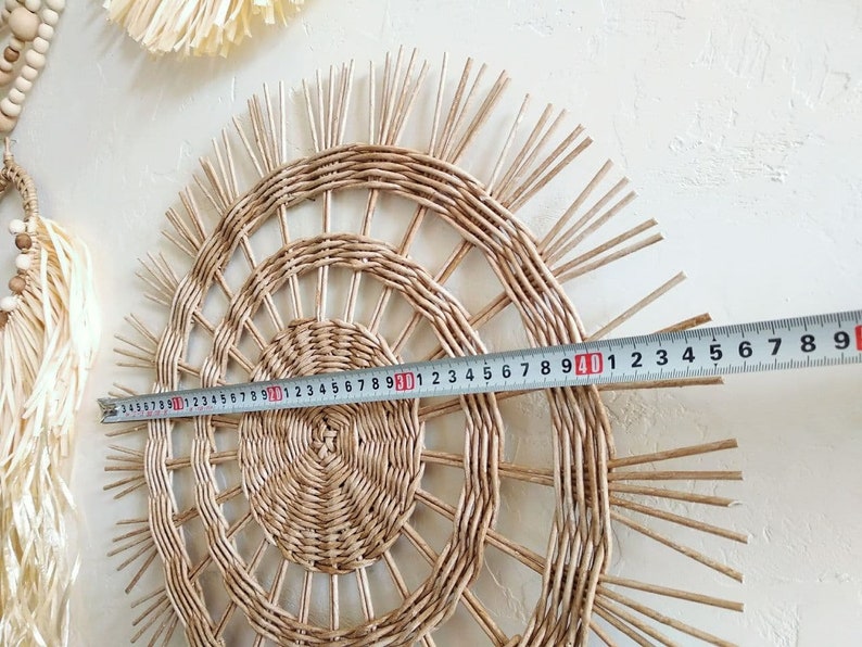 May include: A woven wall hanging with a sunburst design, measuring 40 inches in diameter. The hanging is made of natural materials and has a light brown colour.