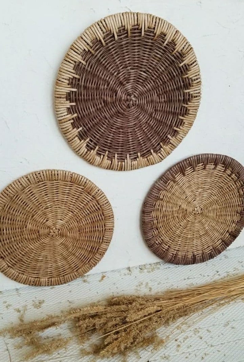May include: Three round woven wall decor pieces in various sizes. The largest piece is brown with a natural woven border. The two smaller pieces are natural woven with a brown border.