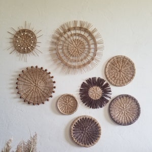 May include: A collection of seven round woven wall decorations in various sizes and patterns. The pieces are made from natural materials and have a rustic, bohemian aesthetic.