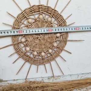 May include: A woven wall hanging in the shape of a sun with wooden beads around the edge. The sun is approximately 20 inches in diameter.