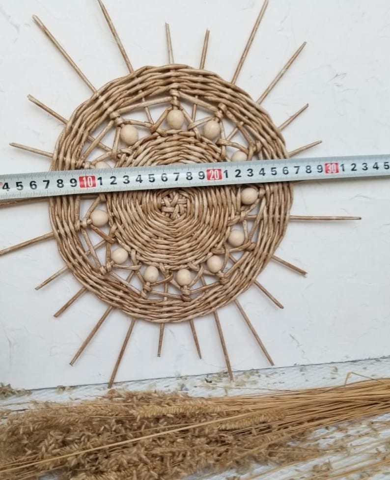 May include: A woven wall hanging in the shape of a sun with wooden beads around the edge. The sun is approximately 20 inches in diameter.