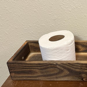May include: A rustic wooden tray with a roll of toilet paper and a wooden sign that says "home".