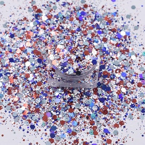 May include: A small jar filled with a variety of glitters in shades of blue, red, silver, and white. The glitter is scattered around the jar on a white surface.
