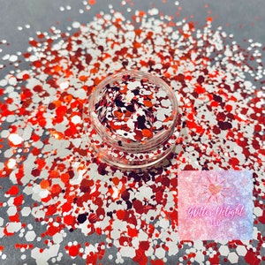 May include: A small jar filled with red and white glitter. The glitter is in various shapes and sizes. The jar is sitting on a gray surface. Glitter Delight LLC is written on a sticker on the jar.