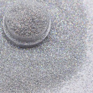 May include: A close-up of iridescent silver glitter in a clear jar. The glitter is very fine and has a shimmery finish.