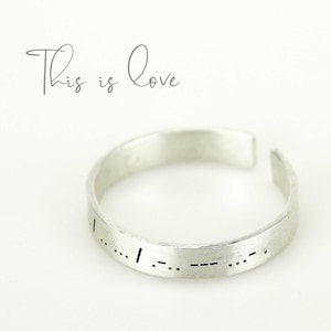 Op de afbeelding: Zilveren ring met de woorden "This is Love" gegraveerd in braille.