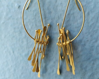 May include: A pair of gold earrings with a geometric design. The earrings are made of thin wire and have a dangling, asymmetrical shape.