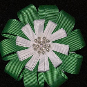 May include: A green and white ribbon bow with a pearl and rhinestone center. The bow is made of multiple layers of ribbon and is tied in a knot.