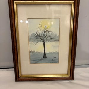 May include: Watercolour painting of a bare tree against a yellow sun and cloudy sky. The artwork is framed in a dark brown wooden frame with a gold inner border. The painting depicts a tranquil, natural scene.