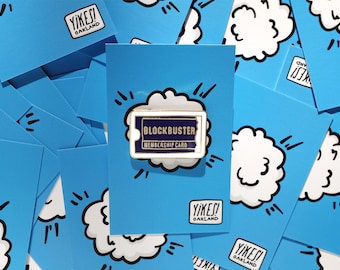 May include: A gold-colored pin with a blue and white design. The pin features the text "Blockbuster Membership Card" in a white font on a blue background. The pin is surrounded by a white cloud with black outlines and black lines radiating from the cloud.