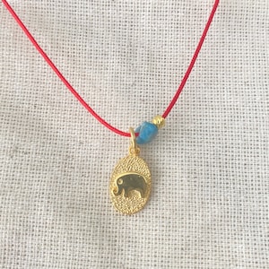 May include: A gold elephant charm necklace with a blue stone bead on a red string.