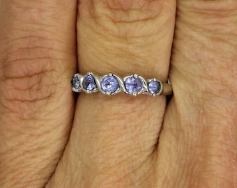 May include: A silver band ring with five purple gemstones set in a wavy pattern.