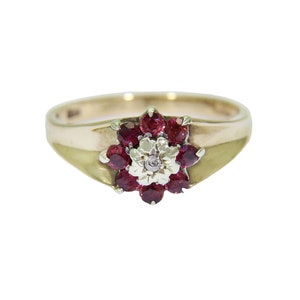 Könnte beinhalten: Ein goldener Ring mit einem Blumendesign aus roten Rubinen und einem Diamanten in der Mitte.