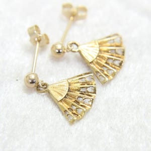 May include: A pair of gold-colored earrings featuring a fan design. Each earring has a post and a small ball, with a fan-shaped pendant. The fan pendants have a detailed, openwork design.