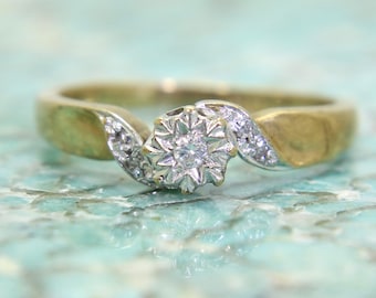 May include: A gold and silver ring with a single diamond in the center and smaller diamonds set around it.