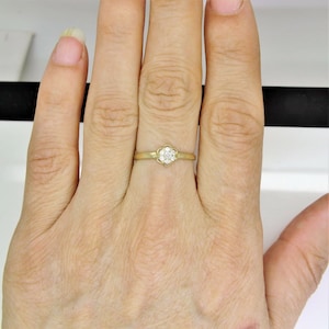 May include: A gold ring with a small flower-shaped setting featuring a cluster of clear diamonds.
