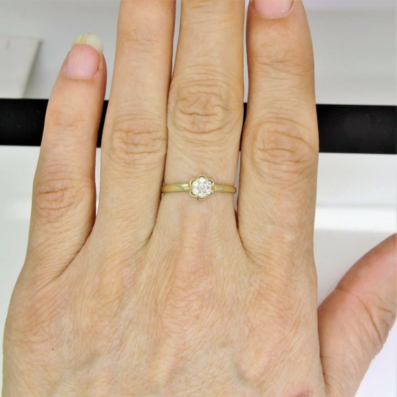May include: A gold ring with a small flower-shaped setting featuring a cluster of clear diamonds.