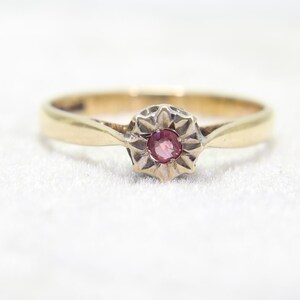 May include: A gold ring with a central, round, pink gemstone. The gemstone is set within a starburst-shaped setting. The band of the ring is a simple, polished gold. The ring is set against a white background.