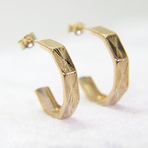 May include: A pair of gold hoop earrings with a geometric design. The earrings are made of a shiny metal and have a simple, elegant style.