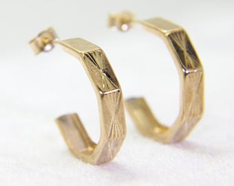 May include: A pair of gold hoop earrings with a geometric design. The earrings are made of a shiny metal and have a simple, elegant style.